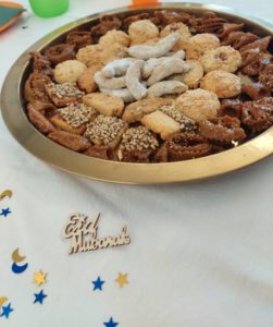 Goldene Flasche Schale mit verschiedenen Gebäcken. Vor der Schale liegt ein aus Holz ausgestanztes "Eid Mabrouk". 