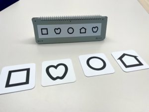 Große Bildkarten mit Symbolen (Quadrat, Herz, Kreis, Haus) vorne, dahinter ein Aufstelltafel zum Umklappen mit den gleichen Symbolen und verschiedenen Zahlen am Rand. 