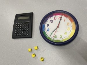 Taschenrechner mit großen Tasten und Bildschirm, Gelbe Würfel mit schwarzen Augen, bunte digitale Wanduhr mit großen Zeigern und Ziffern.