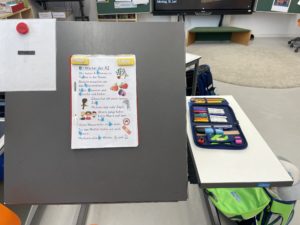 Arbeitsplatz mit magnetischer Tischplatte, schräggestellt, Lesetext in Silbenschrift, daneben vollständiges Mäppchen mit Bunt- und Filzstiften aufgeklappt.