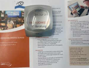 Lupenglas liegt auf Flyer. Text unter dem Lupenglas ist vergrößert sichtbar.