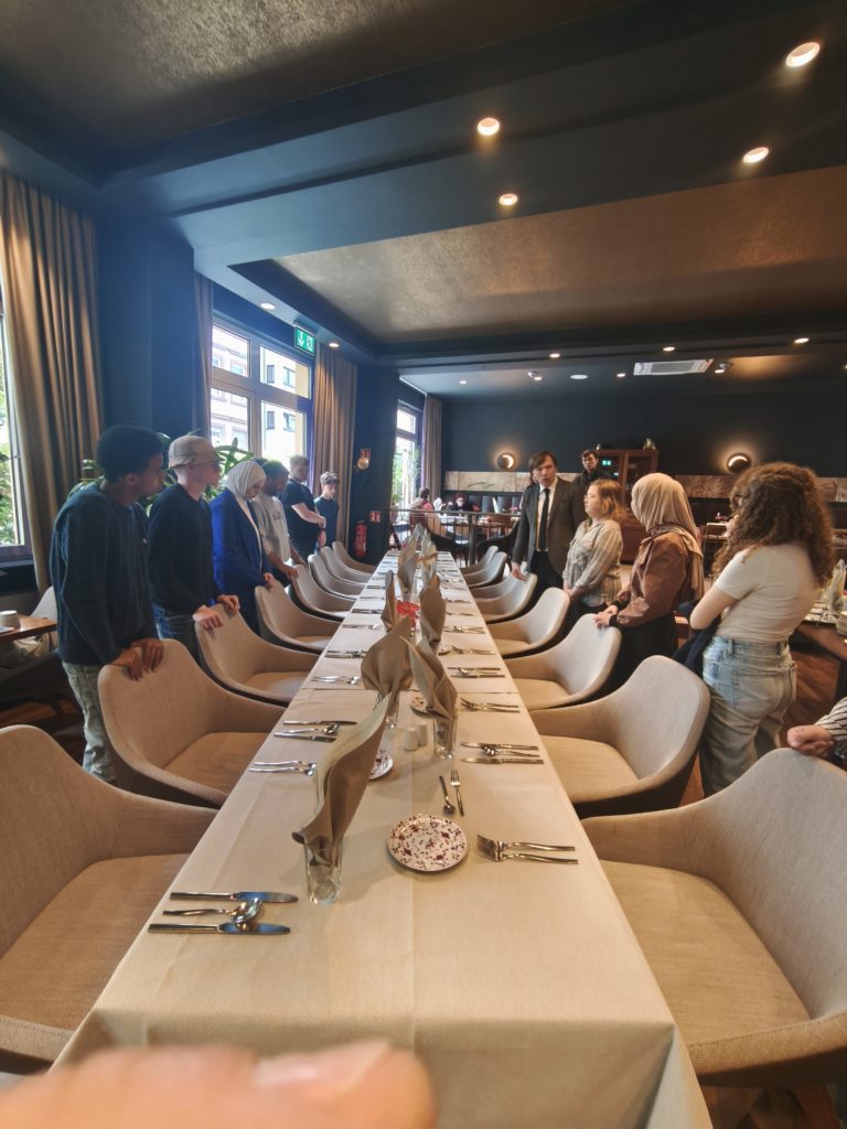 Schülerinnen und Schüler stehen links und rechts neben einer festlich gedeckten Tafel.