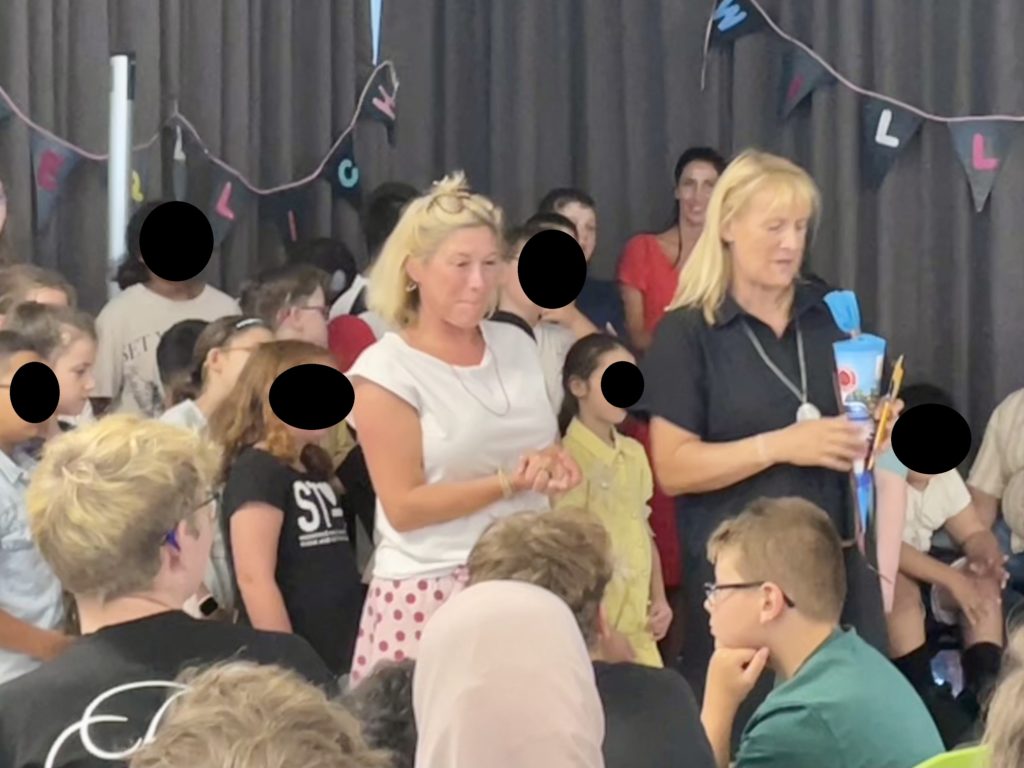 Schulleitung umringt von Schülerinnen und Schülern stehen auf der Bühne
